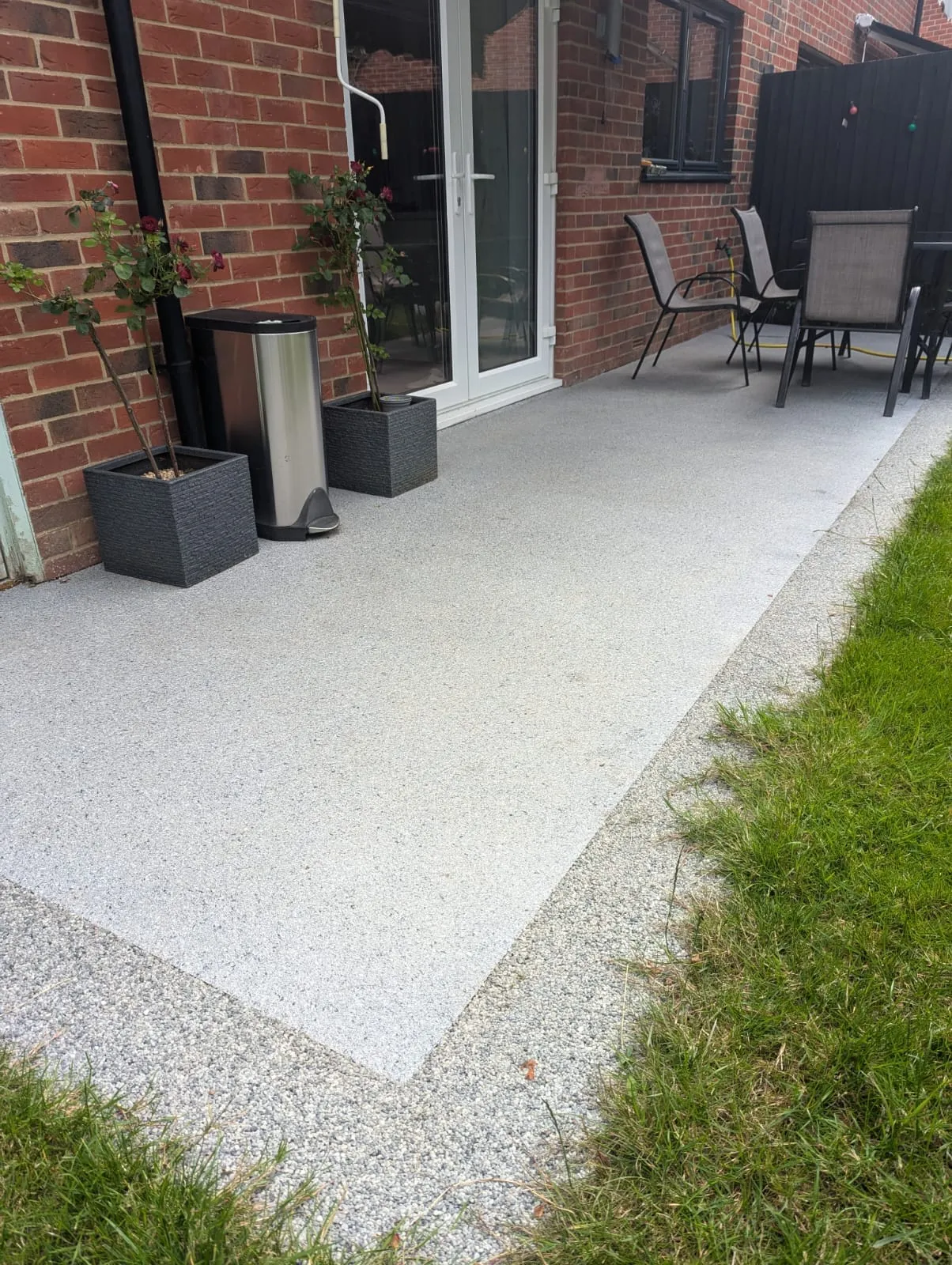 A patio with chairs, a table and a trash can.